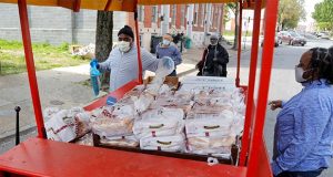 An Arabber, left, hands out free chicken and bread for West Baltimore residents in a horse-drawn cart, Wednesday, April 29, 2020. The 2,000 pounds of frozen chicken, which was donated to the University of Maryland, Baltimore from Holly Poultry, was delivered to residents by the Arabbers, street vendors who sell fruits and vegetables from colorful horse-drawn carts. The university estimated the donation will reach about 900 families as they help battle food concerns during the new coronavirus outbreak. (AP Photo/Julio Cortez)