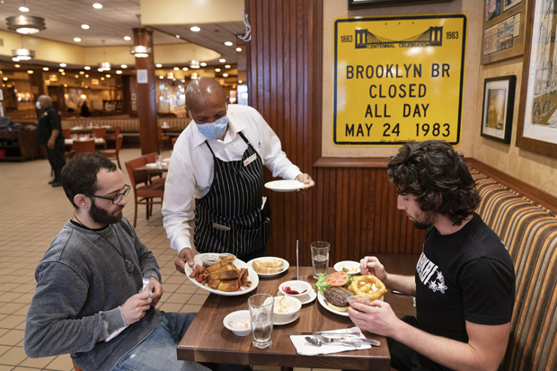 FILE- In this Sept. 30, 2020 file photo, waiter Lenworth Thompson serves lunch to David Zennario, left, and Alex Ecklin at Junior's Restaurant in New York. The U.S. services sector, where most Americans work, registered its fifth consecutive month of expansion in October 2020. (AP Photo/Mark Lennihan, File)