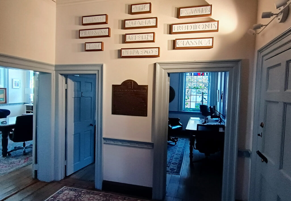 Signs with the Classic Learning Test's name in English, Greek and Latin above a historic marker at the Classic Learning Initiatives headquarters in Annapolis. (Todd Wallack/The Washington Post)