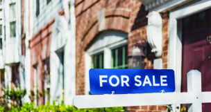 For Sale Sign Hangs in Front of House