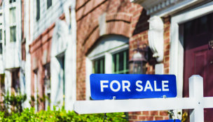 For Sale Sign Hangs in Front of House