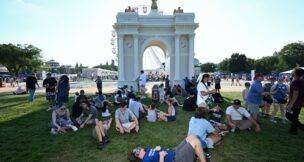 People find shade next to a scaled-down model of an arch proposed by President Donald Trump at the Great American State Fair along the National Mall in July 2026. (Matt McClain/For The Washington Post)