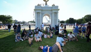 People find shade next to a scaled-down model of an arch proposed by President Donald Trump at the Great American State Fair along the National Mall in July 2026. (Matt McClain/For The Washington Post)